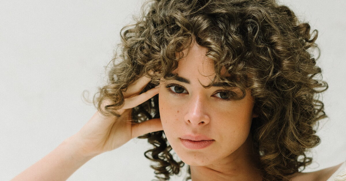 Mujer con cabello rizado y encrespado tratado con productos naturales en peluquería orgánica de Cuenca